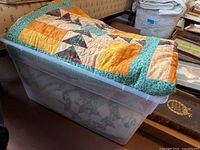 Top view of folded quilt on plastic container showing patchwork colors primarily orange, yellow, and green with paisley print