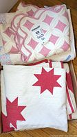 Stack of folded quilts showing white with red stars and pink-white floral patterned quilts