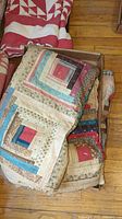 Folded neutral-tone log cabin quilt in cardboard box on hardwood floor