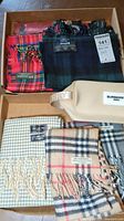 Six scarves arranged in cardboard box showing two on top and three below, plus a Burberry pouch