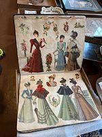 Photo of an open scrapbook showing detailed 19th century fashion illustrations of women dressed in period attire.
