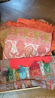 Orange linen with pink and green floral and paisley pattern bordered with fringe, showing wear and some fraying.
