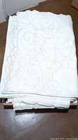 Stack of folded white embroidered tablecloths featuring lace and floral design patterns.