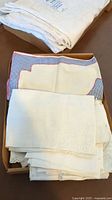 Close-up of folded assorted white and cream table linens including table runners and doilies with various embroidery and lace edges