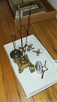Vintage metal receipt holders and multiple antique clock winding keys displayed in a white cardboard tray on wooden floor.