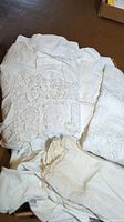 Two white vintage linens with crocheted and embroidered details, showing some damage and wear, folded and placed on a surface.