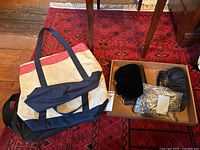 Canvas tote bag with red trim and navy handles beside an open box with several black velvet clutch bags inside.