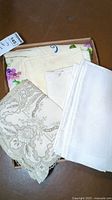 Box containing assorted vintage table linens and napkins of different designs and conditions.