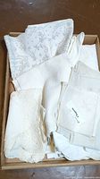 Box of vintage white and off-white tablecloths with lace edges and embroidered floral details visible.
