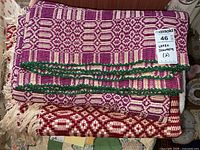 Stacked blankets showing the purple and white blanket on top with green crocheted edge and the red and white blanket underneath with fringes.