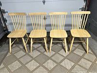 Front view of all four wooden spindle back chairs arranged in a row on a patterned floor.