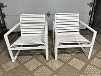 Pair of mid century modern white aluminum frame club chairs with white vinyl straps shown side by side on floor.