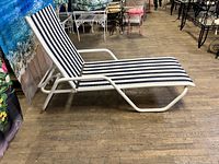 Side angle showing the full length of the chaise lounger with navy and white striped sling on white aluminum frame, placed on wooden floor.