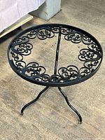 Frontside view of the vintage wrought iron tripod side table highlighting the scrollwork design and overall shape.