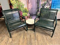Pair of vintage Molla club chairs in garden green with matching small side table between them, displayed on wooden floor with floral backdrop.