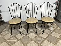 Set of three vintage wrought iron swivel chairs with round padded seats and bronze finish, photographed indoors on patterned floor.