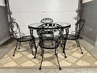 Full view of the complete restored Woodard Chantilly Rose black patio set including one round glass top table and four matching chairs.