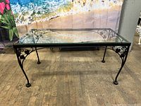 Full view of rectangular wrought iron coffee table with clear glass top showing decorative ivy leaf scrollwork on metal frame and legs.