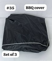 Folded black BBQ grill cover with white piping.
