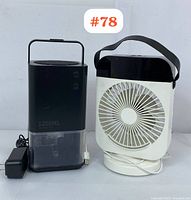 Photo showing the black 1200ml capacity dehumidifier with translucent water tank next to the white and black portable USB cooling fan with handle. Power adapter visible next to dehumidifier.