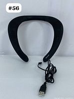 Front view of black Bugani neckband speaker with attached USB charging cable, showing the ergonomic U-shaped design and textured surface.