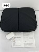 Top view of folded black heated stadium seat cushion with battery pack and printed instruction sheets laid out.