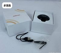 Original white box with Jinghao branding, a small USB charging cable, and a cleaning tool in plastic wrapper seen placed in front of the box.