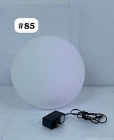 White spherical LED orb light with smooth frosted surface and included black plug-in power adapter placed in front of a white background.