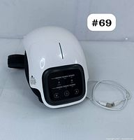 Front angle view of the white knee massager with attached black strap and USB charging cable.