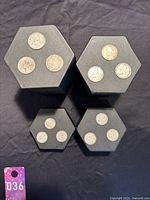 Top-down view of four black hexagonal holders each with 2-3 silver quarters laid on top, showing obverse sides featuring different monarchs.
