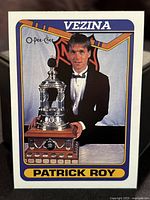 Front of hockey card showing Patrick Roy with Vezina Trophy in tuxedo with blue and yellow border.