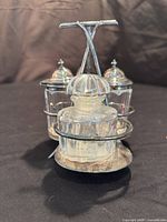 Front view of antique EPNS silver plated condiment caddy with three glass cruets showing design detail and lids.