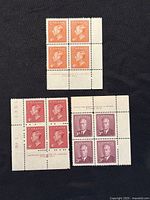 Three plate blocks of Canadian King George VI stamps laid on black background, showing printer's mark and plate numbers on sheet margins