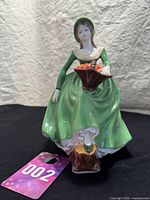 Full view of Coalport Helen bone china figurine standing on a black surface, showing front and side details of green dress and basket.