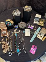 Overall view of lot on black cloth showing all jewelry pieces, watch and pill holder