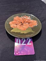 Side angled view of the small circular dish showing raised pink pansy flower design on dark green background.