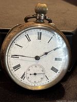 Front view of antique pocket watch showing white enamel dial with Roman numerals and separate small seconds dial at bottom.