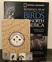 Front view of atlas, logbook front cover, and two bird pins