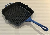 Top view of square blue enamelled cast iron grill pan showing ridged interior, long handle, helper handle