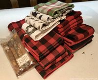 Stacked red and black buffalo check towels, assorted printed and plaid towels, and bag of wine corks