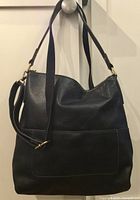 Front view of dark brown Fossil Amelia Hobo leather handbag hanging, showing shape, leather, front pocket, and both straps