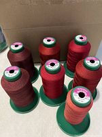 Seven large green-base spools of red Ackermann Isacord thread front view