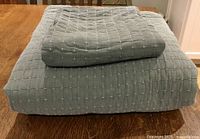 Folded sage green bedspread with pillow sham stacked on wooden surface