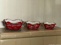 Three red floral stoneware bakers on stand showing graduated sizes