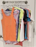 All 13 tops hung on hangers, variety of colours and styles visible