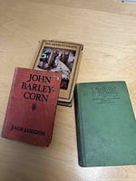 Three hardcover children's books: John Barley-Corn, Treasure Island, and The Arabian Nights arranged on a wood surface.