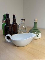Full set of all five items: three beer bottles (two brown, one green), skull bottle, olive oil decanter, and white gravy boat on wood surface.