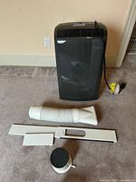 Portable air conditioner unit with exhaust hose, window panels, circular adapter and remote laid out on carpet