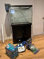 Large glass aquarium on black stand with assorted aquarium accessories placed in front on floor including boxes and hose.