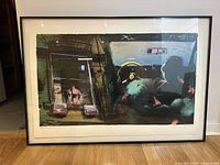 Framed silkscreen print leaning against a wall on a wooden floor showing the entire artwork and frame.